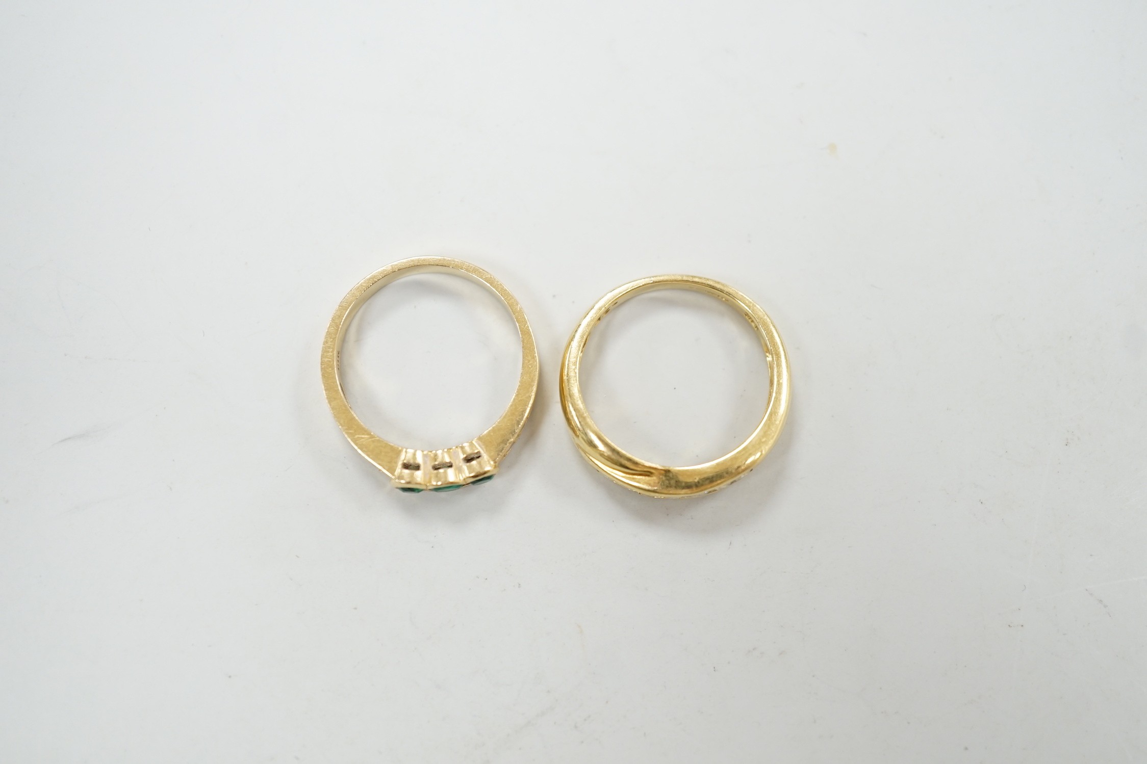 A modern 18ct gold and cannel set seven stone diamond crossover ring, size O and a similar 18k, three stone emerald and four stone diamond chip set ring, size N/O, gross weight 7.8 grams.